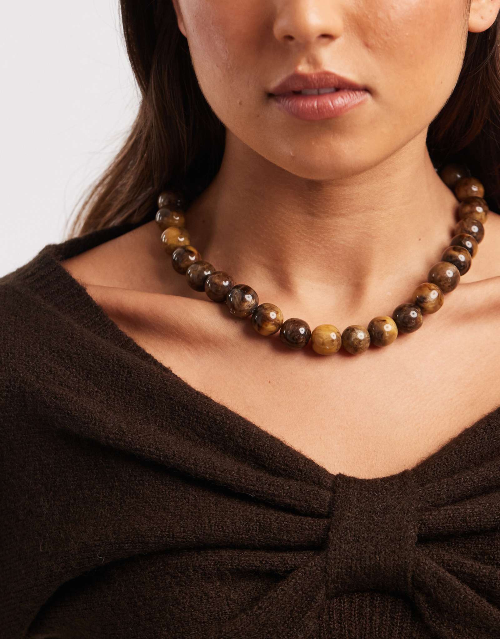 Дополните ожерелье из коричневых бусин из смолы аксессуарами в золоте