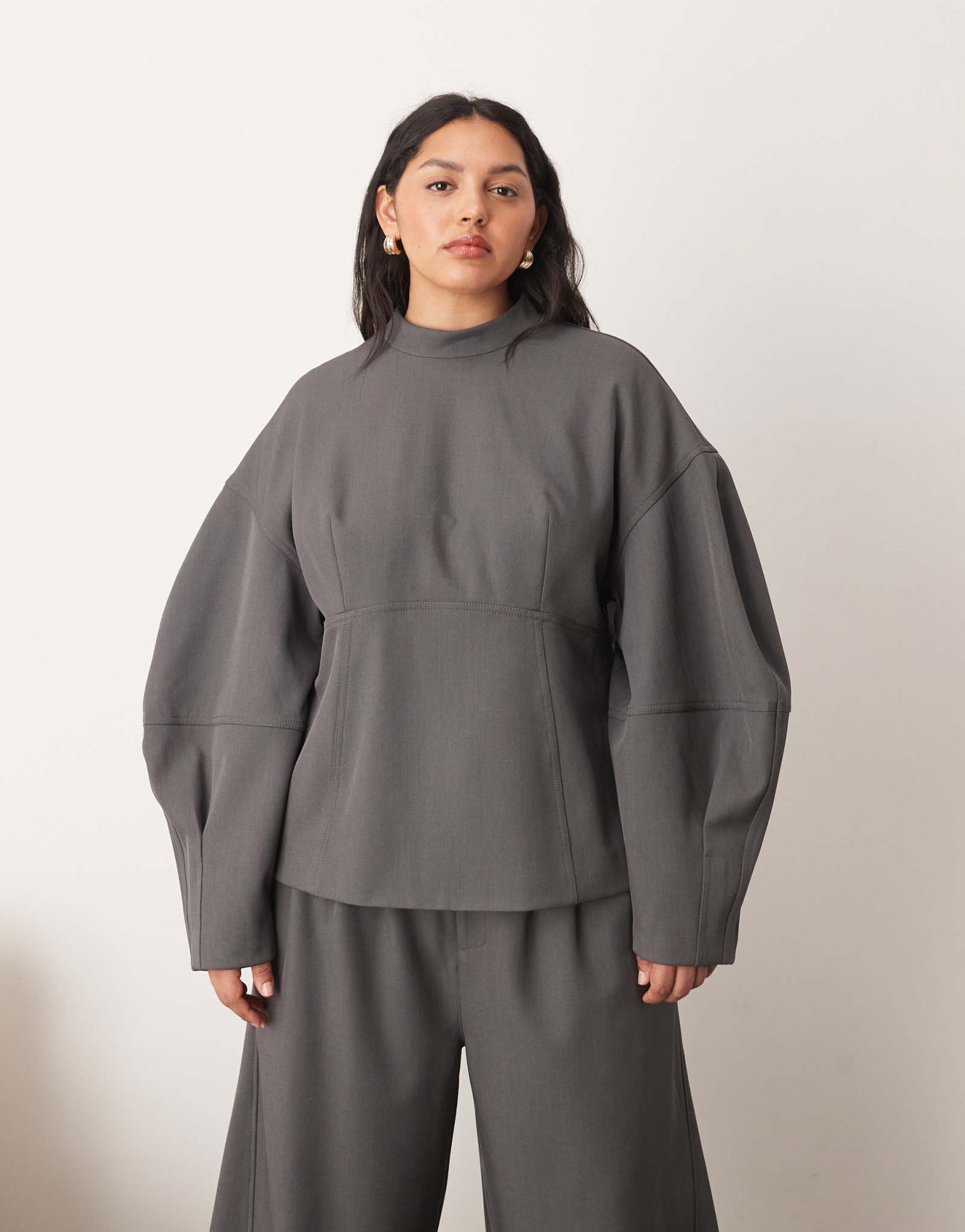 Облегающий топ с овальными рукавами серого цвета, выполненный в виде скроенного по фигуре шва, является частью комплекта