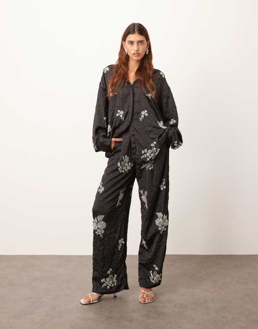 ARRANGE - Pantaloni neri in raso stropicciato decorati a fiori in coordinato