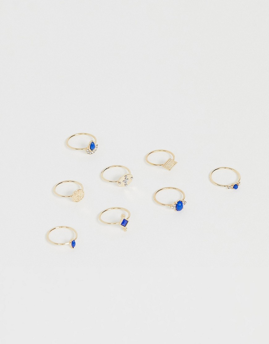 ASOS DESIGN – 8-pack guldfärgade ringar med graverade mynt och blå stenar