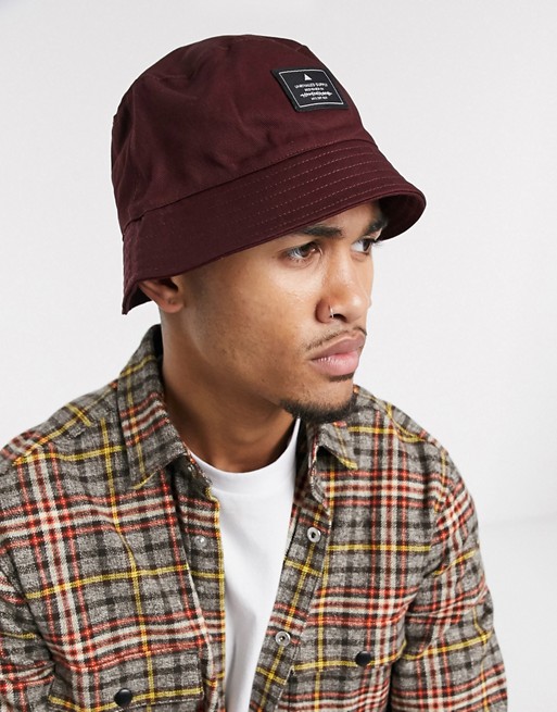 ASOS Unrvlld Supply bucket hat in burgundy with branded patch