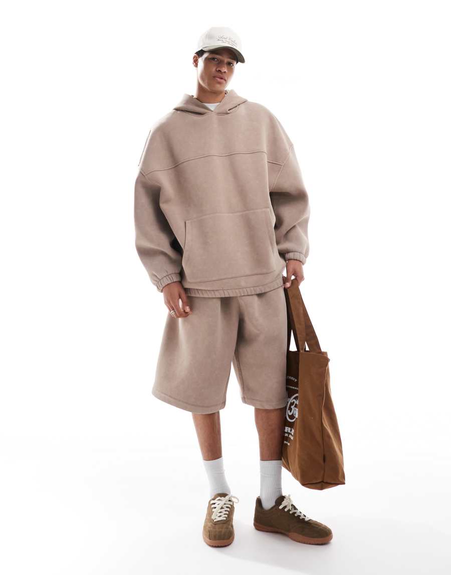 Washed-beige oversized hoodie and matching knee-length shorts with a pale cap, white socks, brown suede sneakers and a brown tote