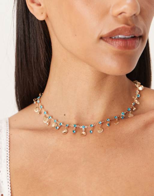 ASOS DESIGN - Collana con conchiglie piccole color oro e cristalli sintetici blu
