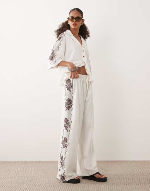 ASOS DESIGN - Coordinato in jersey testurizzato color crema con conchiglie ricamate composto da polo e pantaloni a fondo ampio