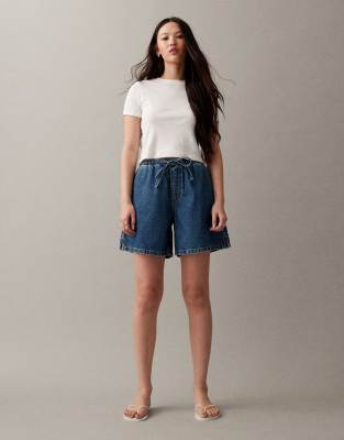 ASOS DESIGN - Länger geschnittene Schlupf-Jeansshorts in Mittelblau