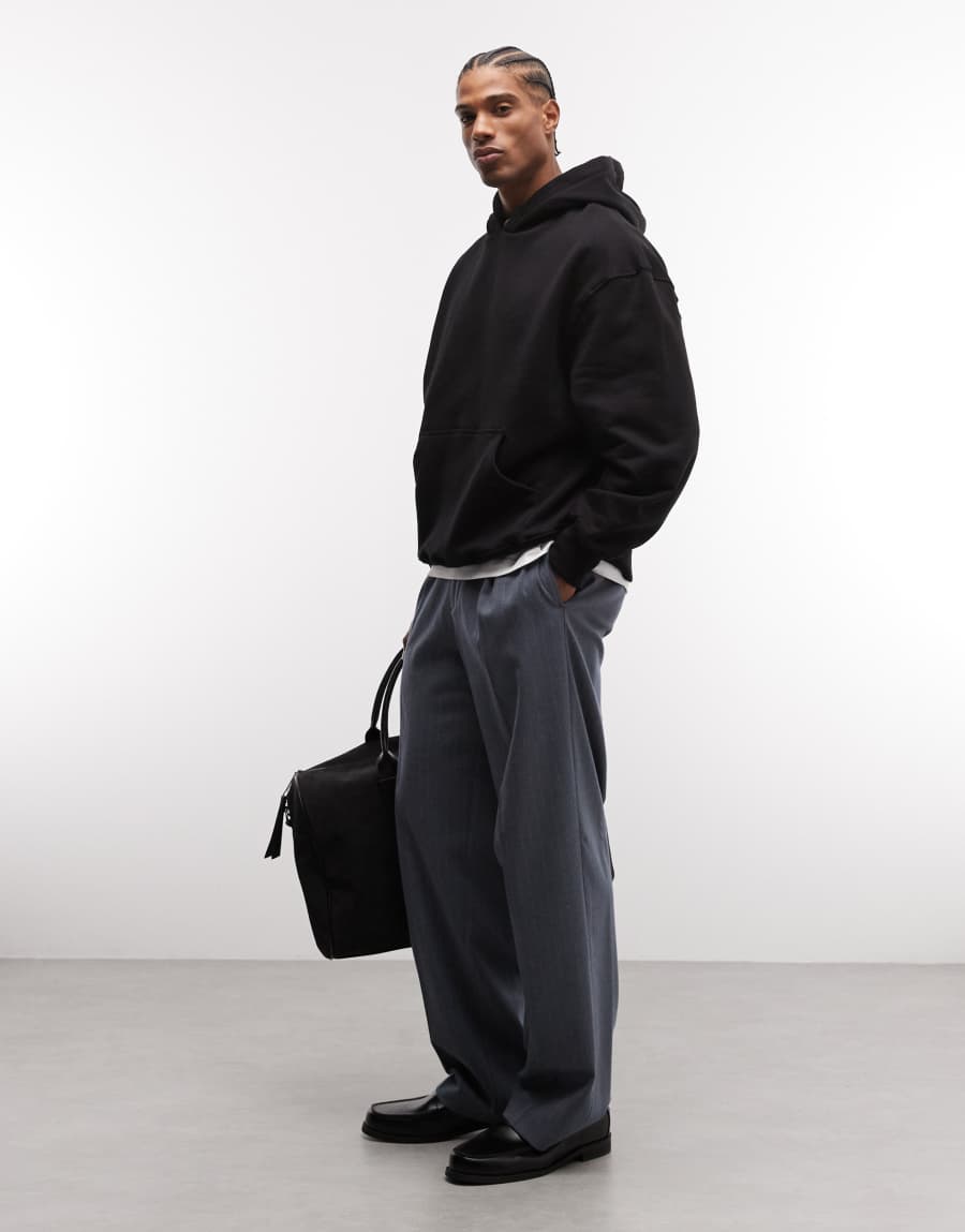 Black oversized hoodie over a white T-shirt, with wide gray trousers, black leather loafers and a black tote