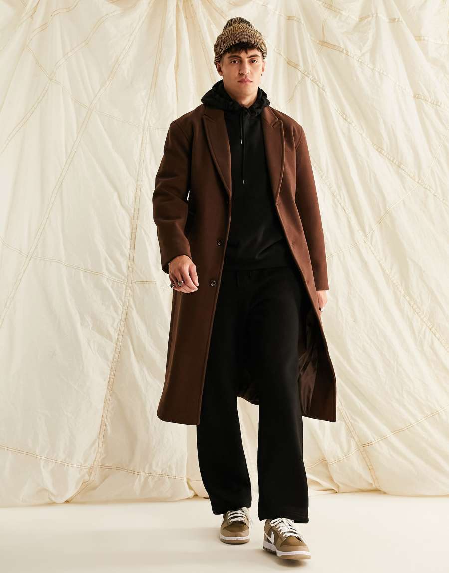 Brown overcoat over a black hoodie and loose black pants, with a brown beanie and brown-and-white sneakers