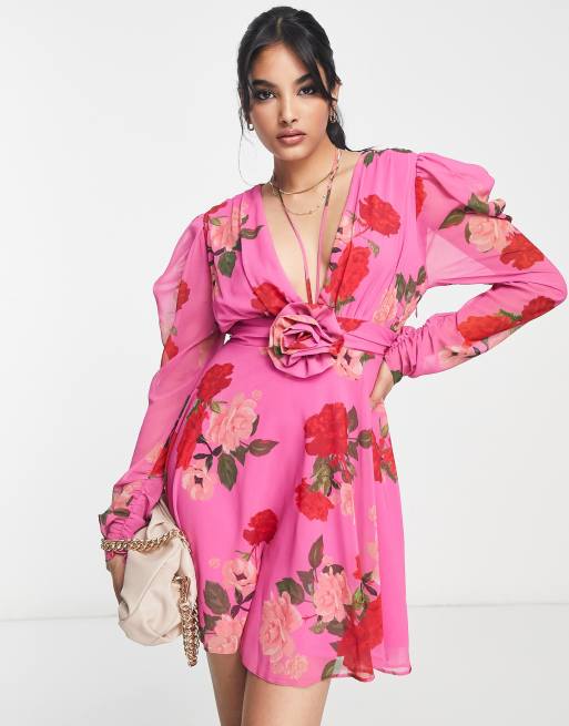 ASOS DESIGN – Różowa sukienka mini z długimi rękawami, wiązaniem na szyi i ozdobą w kształcie kwiatu w kwiatowy wzór 
