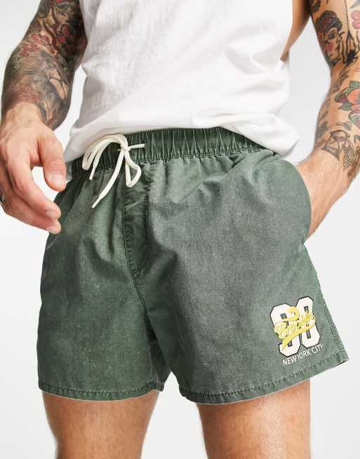 ASOS DESIGN swim shorts in short length with collegiate print in dark green acid wash