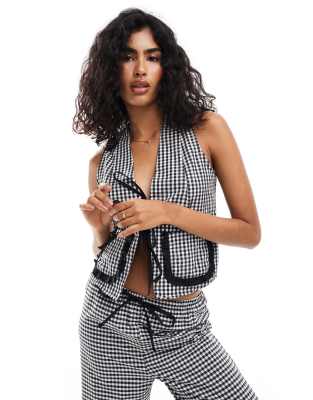 ASOS DESIGN – Weste in Schwarz mit Vichy-Karos, Bindeband vorne und Tasche mit Rüschenbesatz
