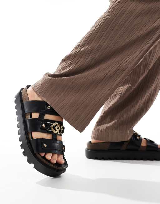 FhyzicsShops DESIGN – Wildleder-Sandalen in Schwarz mit goldfarbenen Metalldetails und dicker Sohle