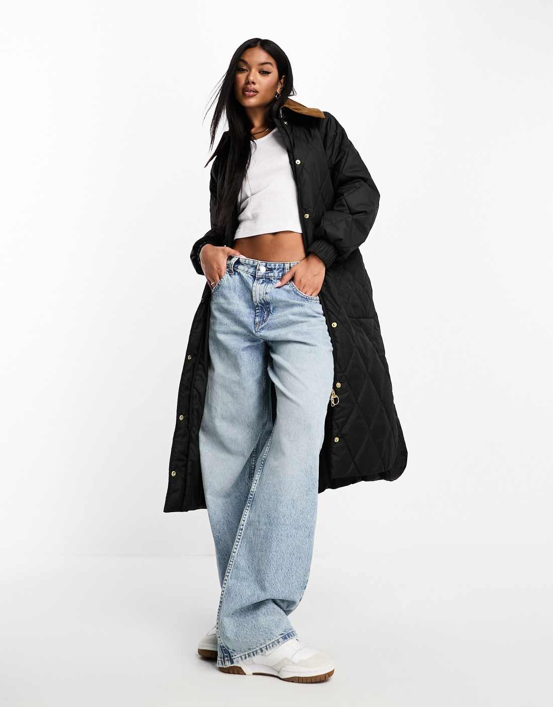 Long black diamond-quilted coat worn open over a white top, loose blue jeans and sneakers