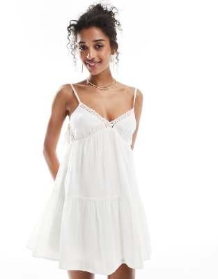 Bershka - Gestuftes Minikleid in Weiß mit Riemchenträgern und Spitzenbesatz