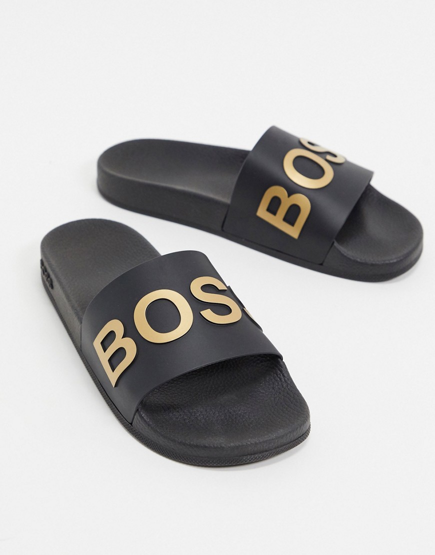 BOSS – Bay – Svarta och guldfärgade tofflor