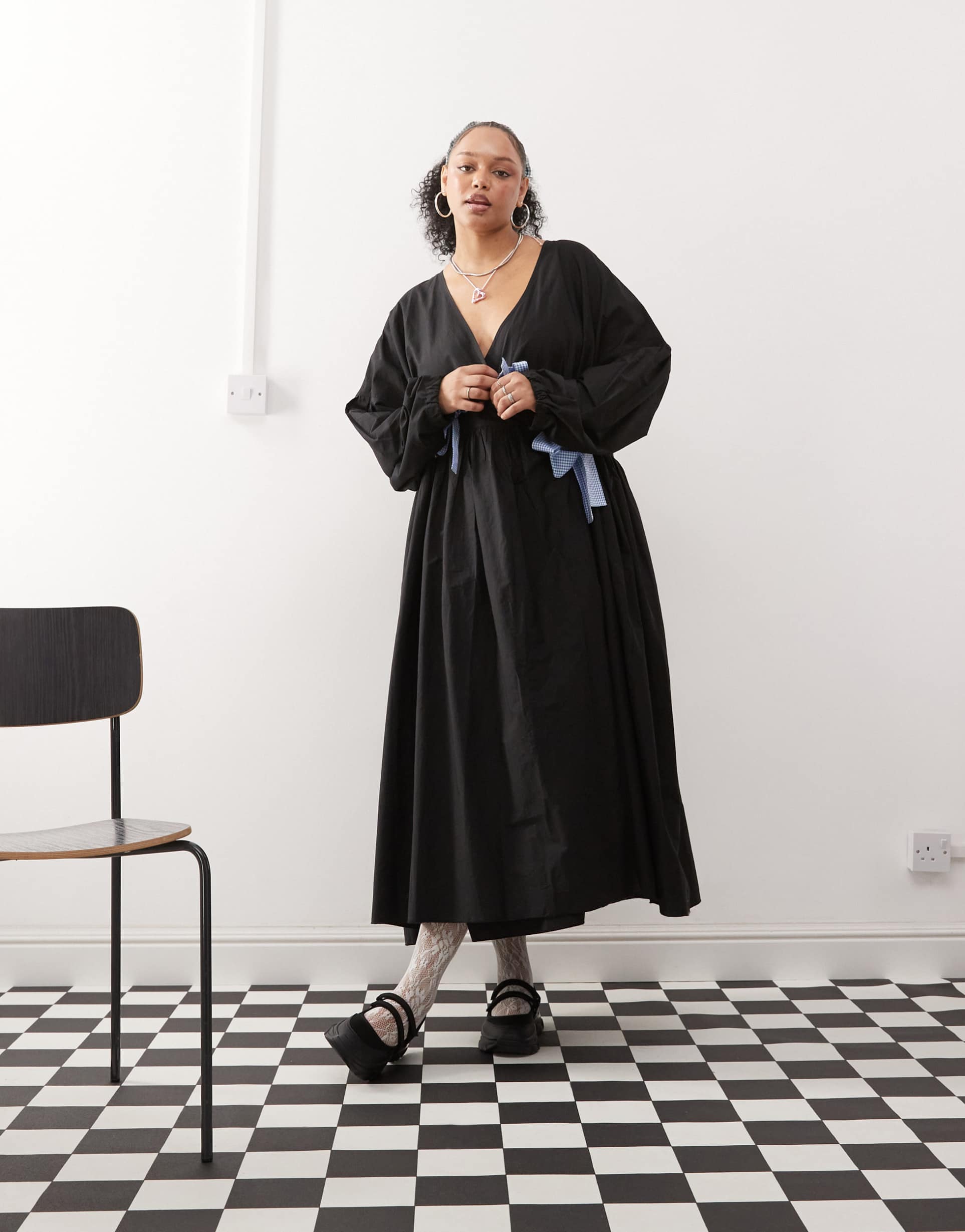 A long-sleeve, plus-size, black wrap midaxi dress with light blue gingham bows