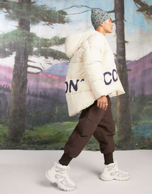 COLLUSION Unisex - Oversized gewatteerd jack met print en grote capuchon in ecru