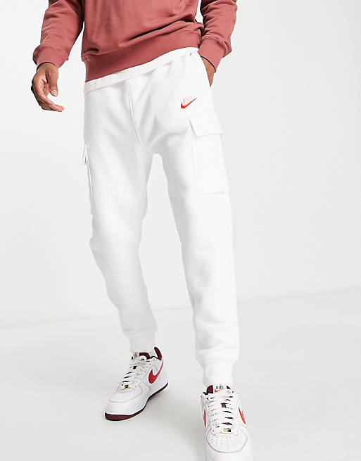 Hombre Joggers de ropa deportiva | Joggers blancos cargo con logo rosa de felpa de Nike Club - XG25378