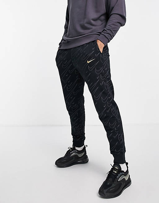 Nike all over swoosh print cuffed joggers in black and gold | ASOS