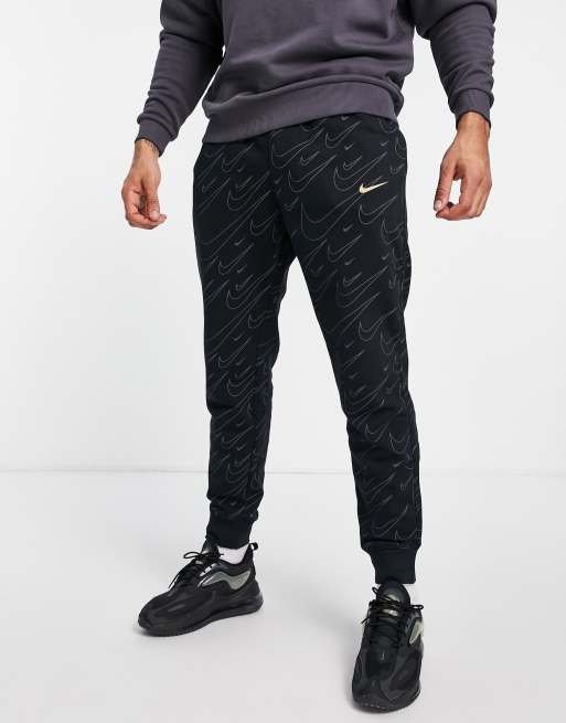 Nike all over swoosh print cuffed joggers in black and gold ASOS