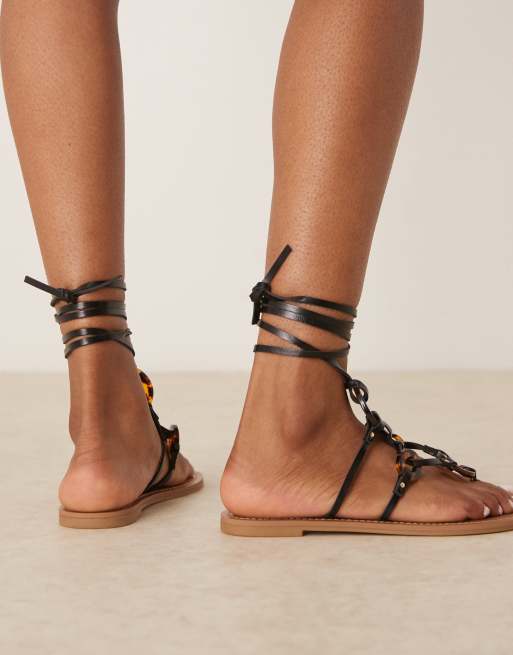 Sandalias negras planas con diseño anudado a la pierna y detalles