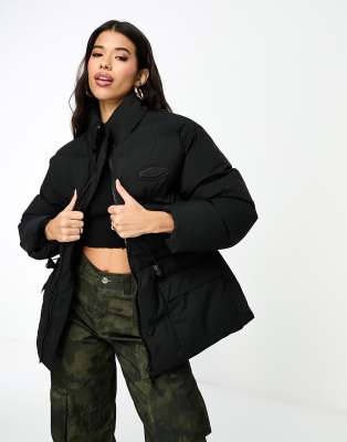 The Couture Club - Plissierte Oversize-Pufferjacke in Schwarz mit Bindegürtel