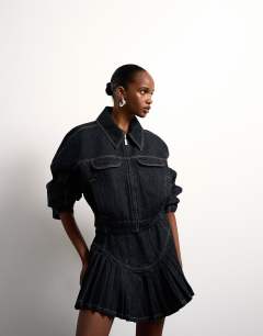 Model wearing Tolu Coker x Topshop denim super mini pleated skirt circular design in deep blue
