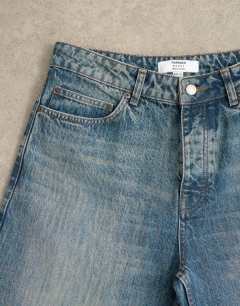 Model wearing Circular design rigid baggy jean in mid wash tint