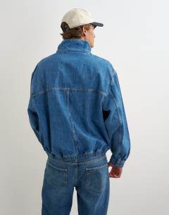 Model wearing Oversized fit denim jacket with funnel neck in mid wash