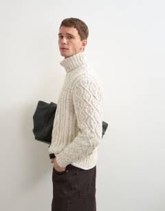 Model wearing Relaxed fit cable knitted roll neck jumper in ecru