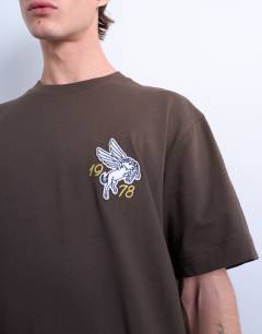 Model wearing Relaxed Pegasus embroidered t-shirt with back text in brown