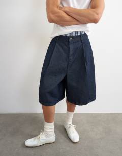 Model wearing Wide leg denim bermuda short with pronounced pleat in mid-wash blue