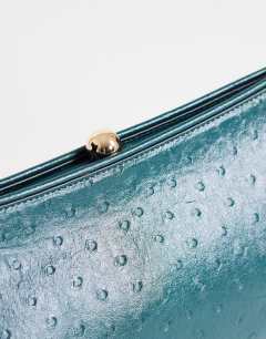 Model wearing Alice medium clutch bag in teal ostrich