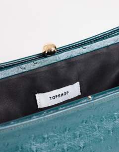 Model wearing Alice medium clutch bag in teal ostrich