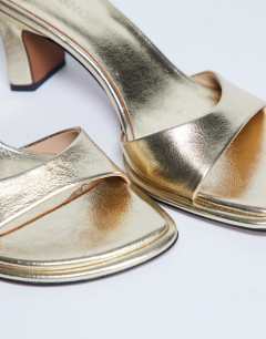 Model wearing Ari mule mid heeled sandal in gold