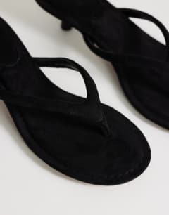 Model wearing Axel toe thong mid heel sandal in black faux suede 