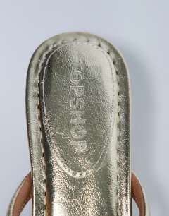 Model wearing Axel toe thong mid heel sandal in gold