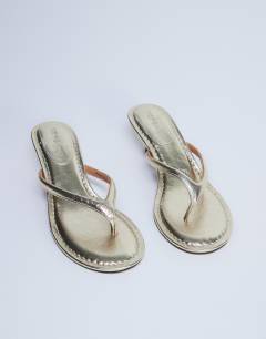 Model wearing Axel toe thong mid heel sandal in gold