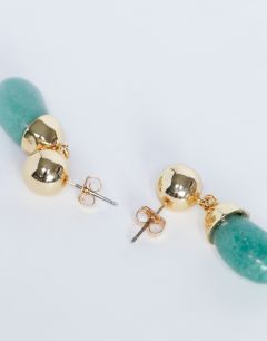 Model wearing Blaze stud earrings with drop design in gold and green