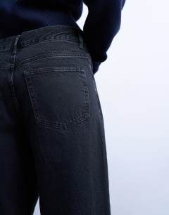 Model wearing Column mid rise jean with rip in washed black