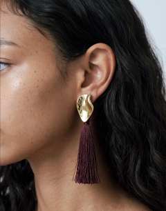 Model wearing Emil studded statement tassel earrings in burgundy and gold