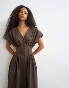 Model wearing Exaggerated shoulder cinched pintucked waist maxi dress in chocolate brown with contrast topstitching