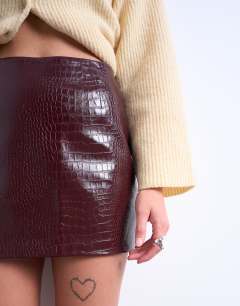 Model wearing Faux snake patent leather mini skirt in burgundy