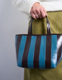 Model wearing Gemma stripe faux leather grab bag in blue and brown
