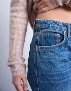 Model wearing Hourglass Ember low rise straight leg jean in mid blue