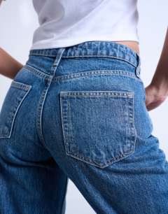 Model wearing Hourglass Ember low rise straight leg jean with knee rip in mid blue
