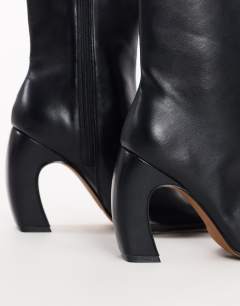 Model wearing Karter curved heel ankle boot in black stretch faux leather