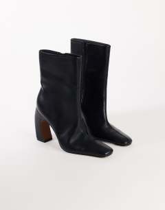 Model wearing Karter curved heel ankle boot in black stretch faux leather