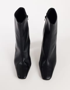 Model wearing Karter curved heel ankle boot in black stretch faux leather