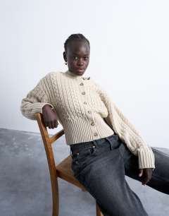 Model wearing Knitted cable fitted waist cardigan in oat