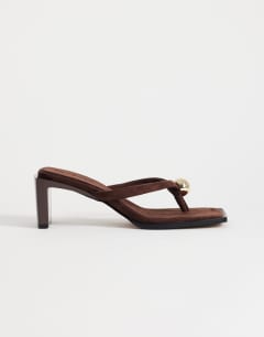 Model wearing Nadeem mid heel toe thong sandal with hardware in chocolate